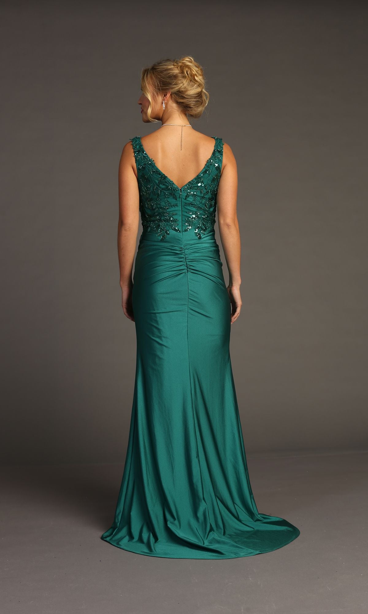 A woman stands facing away in the Sequin-Bodice Long Prom Dress: Chicas YG5032—an emerald green gown with a fitted, beaded bodice and a V-shaped back, perfect for any formal occasion.